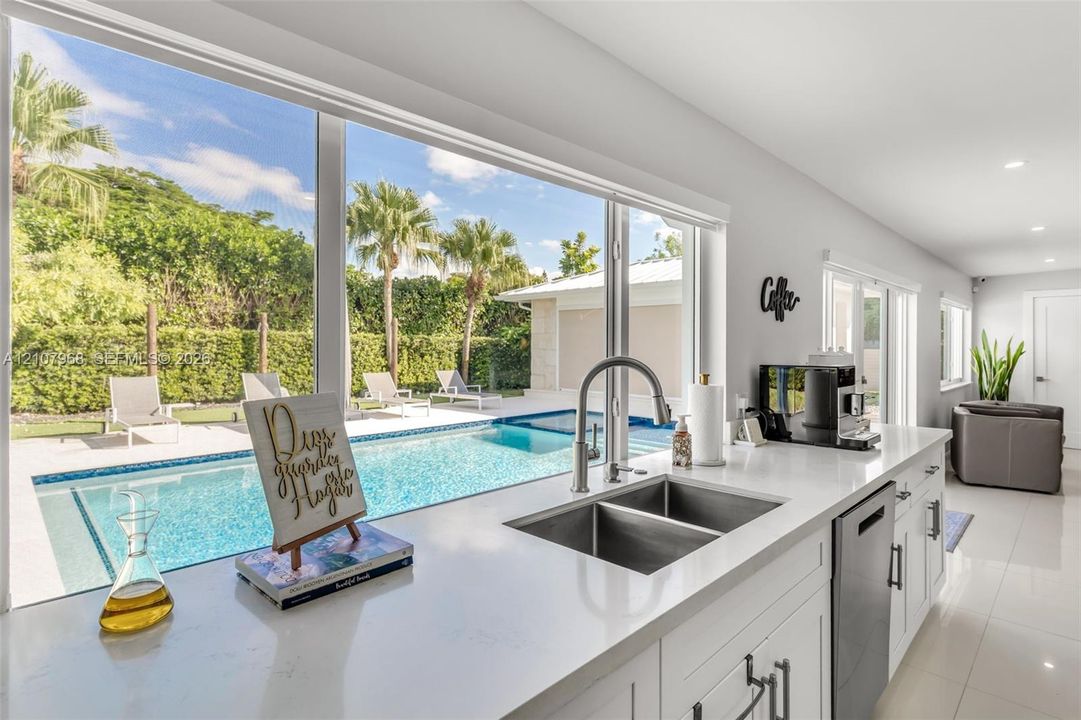Kitchen featuring expansive windows, white cabinetry, quartz countertops, dual-basin stainless steel sink, and stainless steel dishwasher