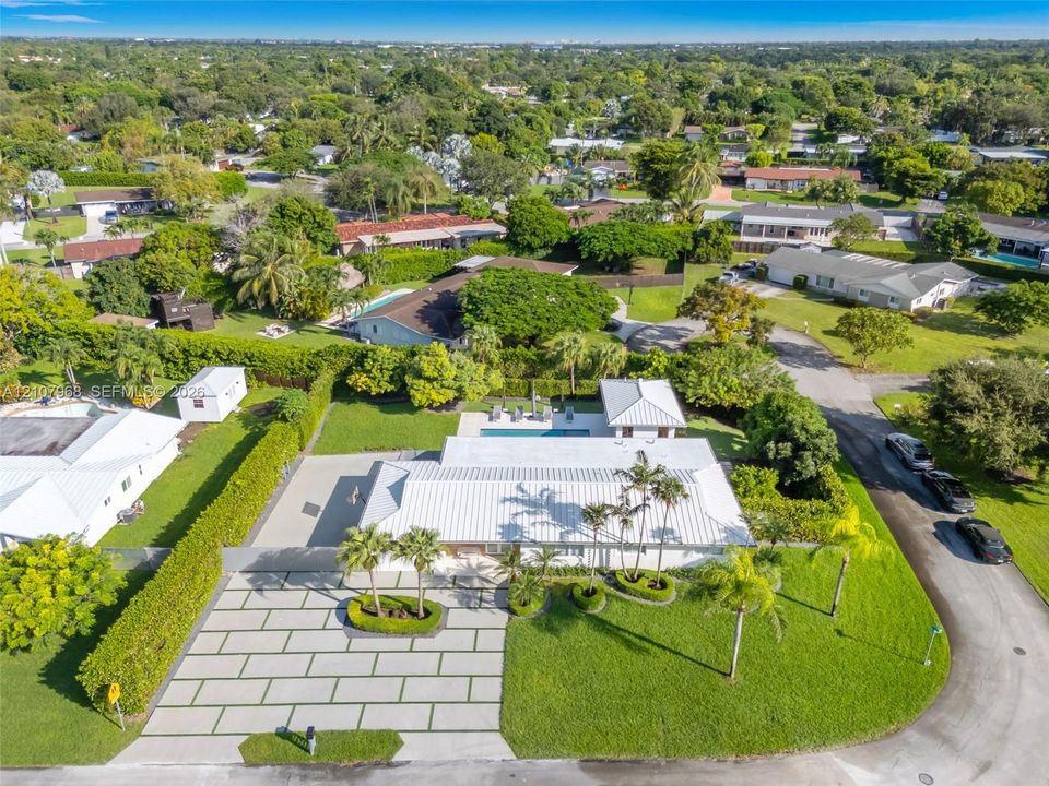 Aerial perspective featuring a metal roof, paved geometric driveway, swimming pool, detached structure, and mature landscaping