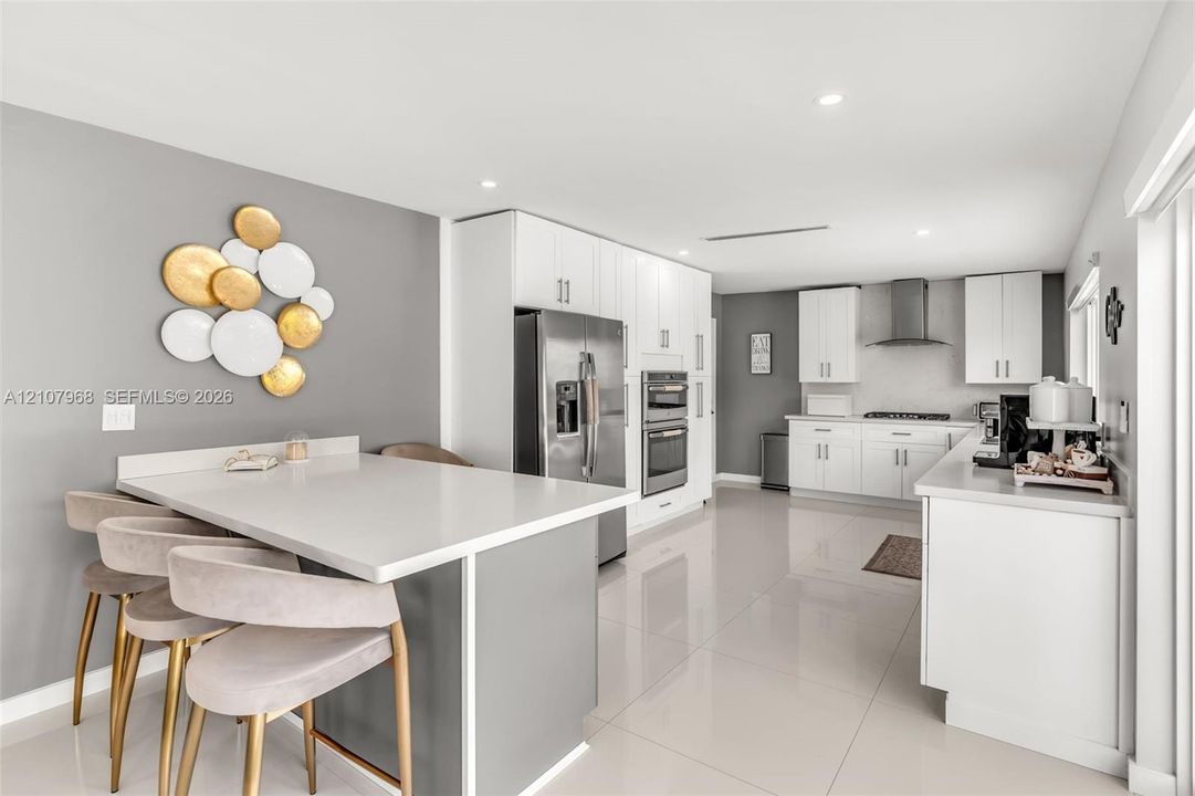 Kitchen featuring white shaker-style cabinetry, quartz countertops, stainless steel appliances, recessed lighting, and large-format porcelain tile flooring