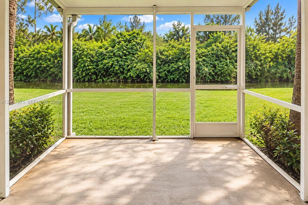 Screened-in patio with concrete flooring, aluminum framing, and a full-height entry door, overlooking a lawn and waterfront