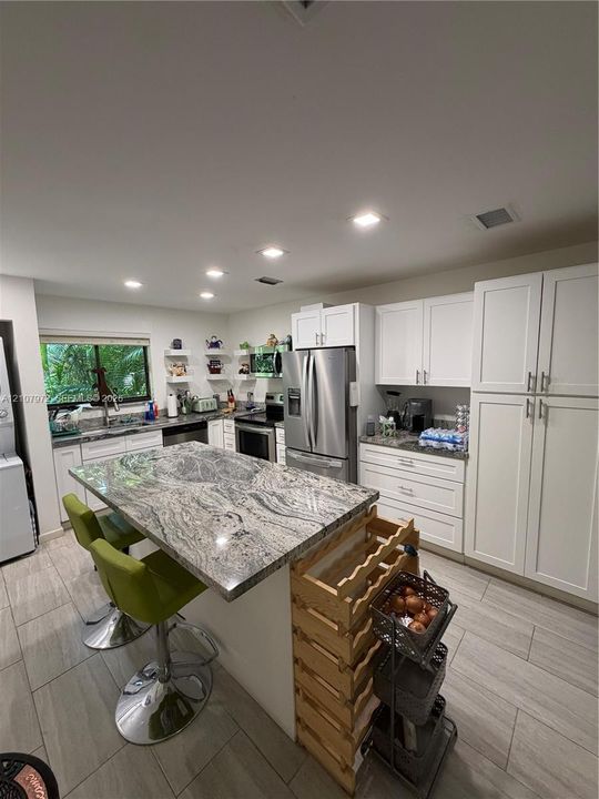 Kitchen featuring a stone-topped central island, recessed ceiling lighting, white cabinetry, stainless steel appliances, and wood-finish flooring