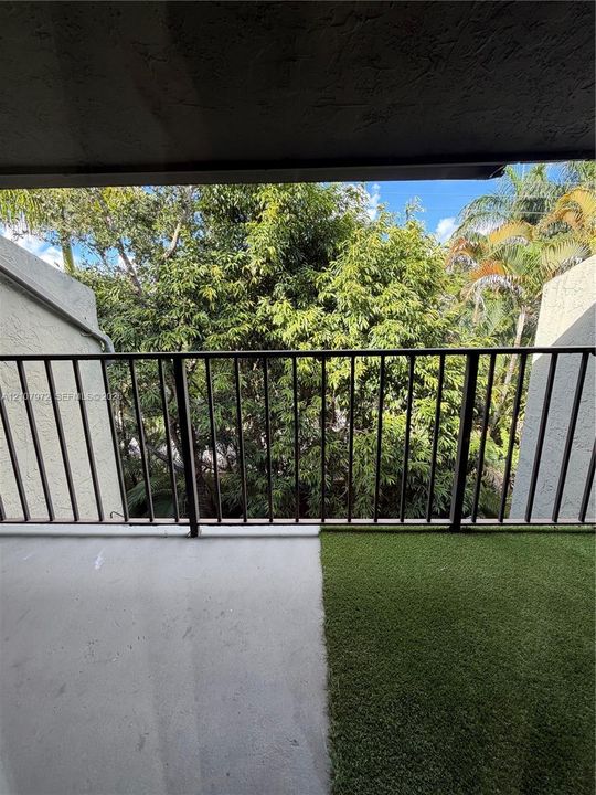 Covered balcony featuring concrete flooring, artificial turf, and metal railing