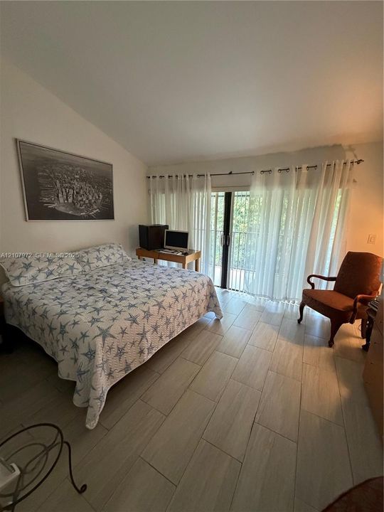 Room featuring a vaulted ceiling, wood-finish tile flooring, and glass sliding doors providing access to an exterior balcony