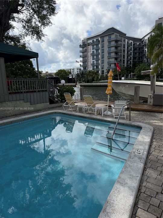 In-ground swimming pool with built-in stairs, concrete paver decking, and a private wooden dock situated on a waterway