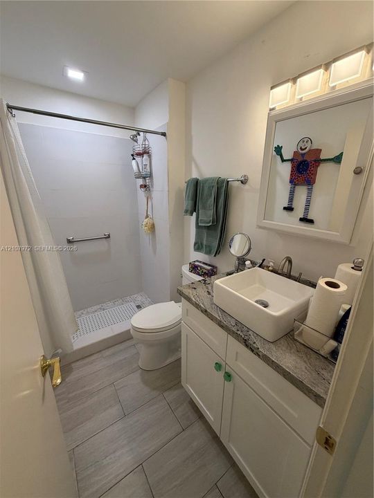 Bathroom featuring a stone-surface vanity with a rectangular vessel sink, white cabinetry, tile flooring, and a walk-in shower with a mosaic-tile floor
