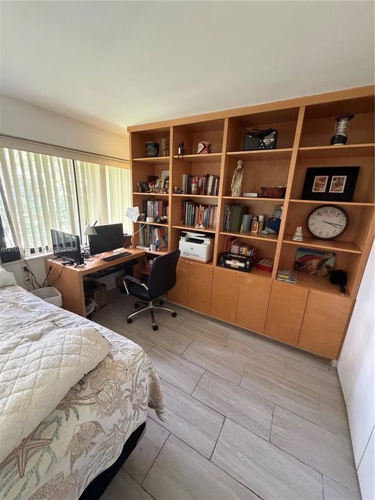 Floor-to-ceiling custom wood cabinetry featuring integrated shelving, built-in desk workspace, wood-finish tile flooring, and large window with vertical blinds