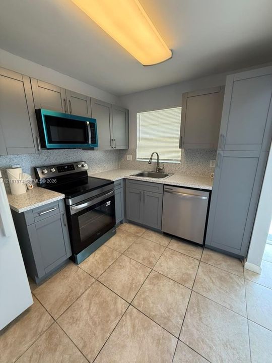 Kitchen featuring grey shaker-style cabinetry, speckled countertops, stainless steel appliances, a stainless steel sink with a high-arch faucet, and ceramic tile flooring