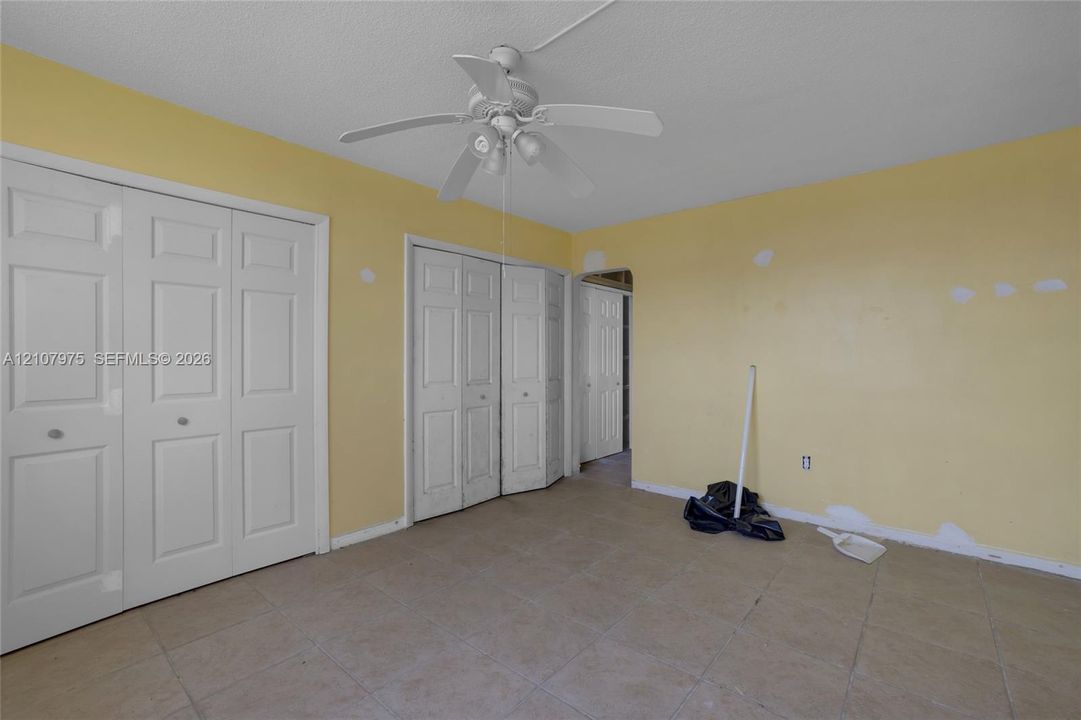 Room featuring ceramic tile flooring, a white ceiling fan with integrated lighting, and two sets of bi-fold closet doors