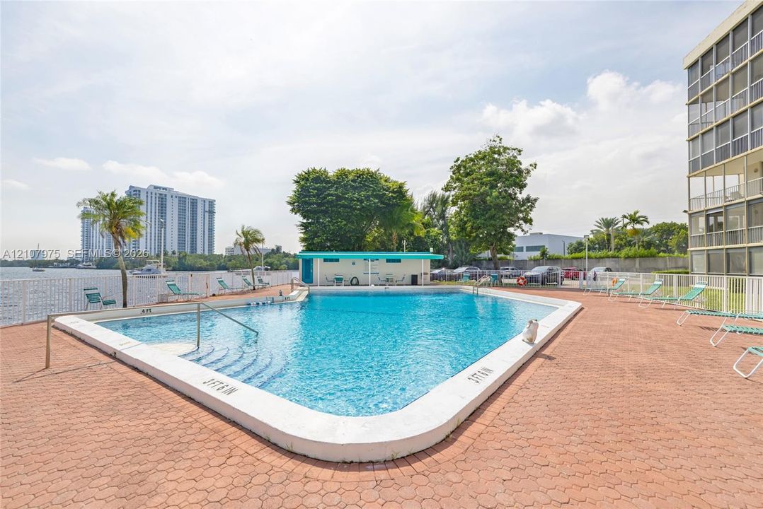 Outdoor swimming pool featuring a brick paver deck, metal perimeter fencing, and an on-site cabana