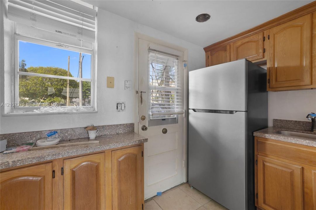 Kitchen featuring solid wood cabinetry, stone-finish countertops, stainless steel refrigerator, and a dedicated entry door with integrated window blinds