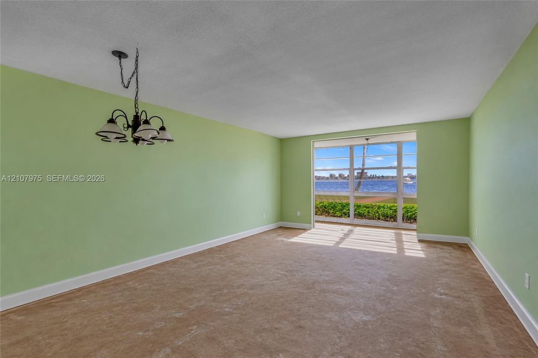 Spacious room featuring floor-to-ceiling windows with water exposure, wall-to-wall carpeting, and a multi-arm metal chandelier