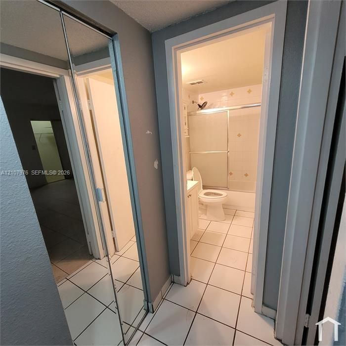 Full-height mirrored sliding closet doors and white ceramic tile flooring
