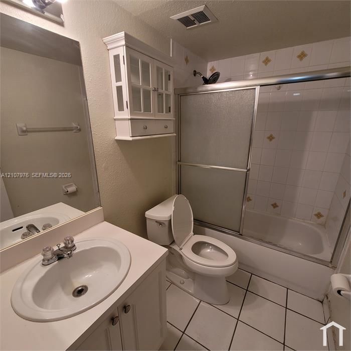 Bathroom featuring a vanity with an integrated basin, a wall-mounted glass-front cabinet, a shower-tub combination with sliding glass doors, and tiled flooring