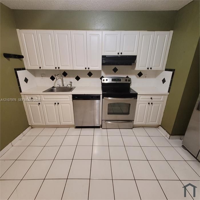 Kitchen featuring white shaker-style cabinetry, stainless steel dishwasher and range, solid-surface countertops, and ceramic tile flooring