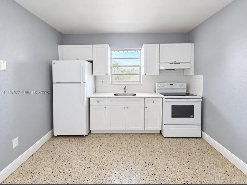Kitchen featuring white cabinetry, solid-surface countertops, subway tile backsplash, white appliances, and terrazzo flooring