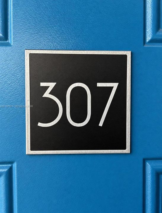 Square metallic unit signage featuring crisp white lettering mounted on a blue paneled door