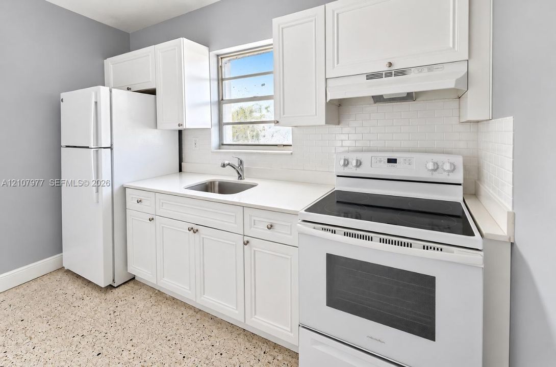 Kitchen featuring white shaker-style cabinetry, solid-surface countertops, a subway tile backsplash, terrazzo flooring, and stainless steel undermount sink