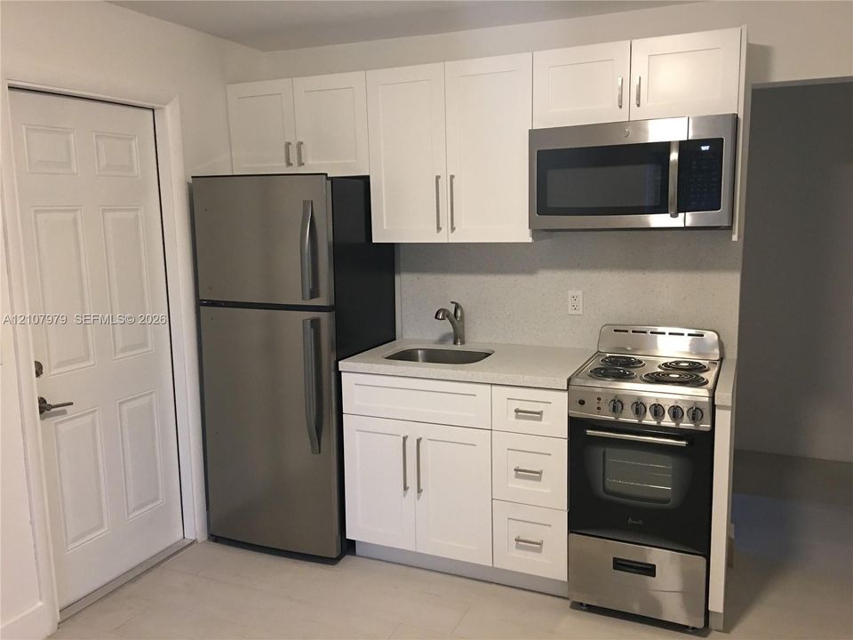 Kitchen area featuring white shaker-style cabinetry, solid-surface countertops, a stainless steel refrigerator, an over-the-range stainless steel microwave, and a stainless steel electric range