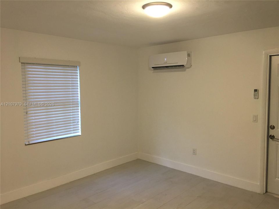 Interior space featuring wood-finish flooring, a wall-mounted ductless mini-split air conditioning unit, a window with horizontal blinds, and a flush-mount ceiling light fixture