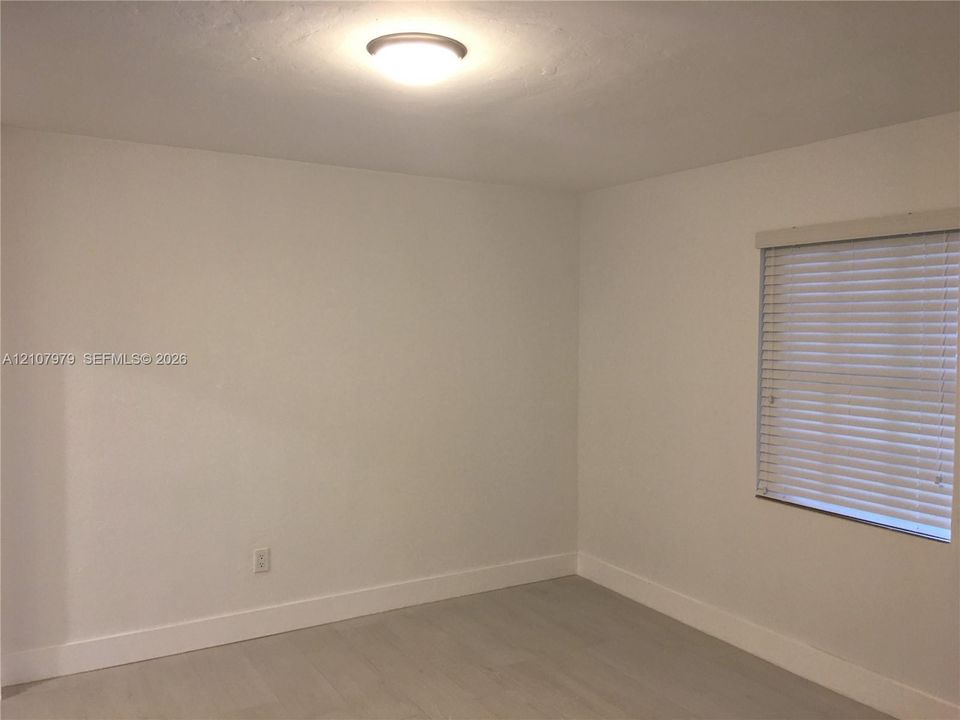 Room with neutral walls, light-toned wood-finish flooring, flush-mount ceiling light, and window with horizontal blinds