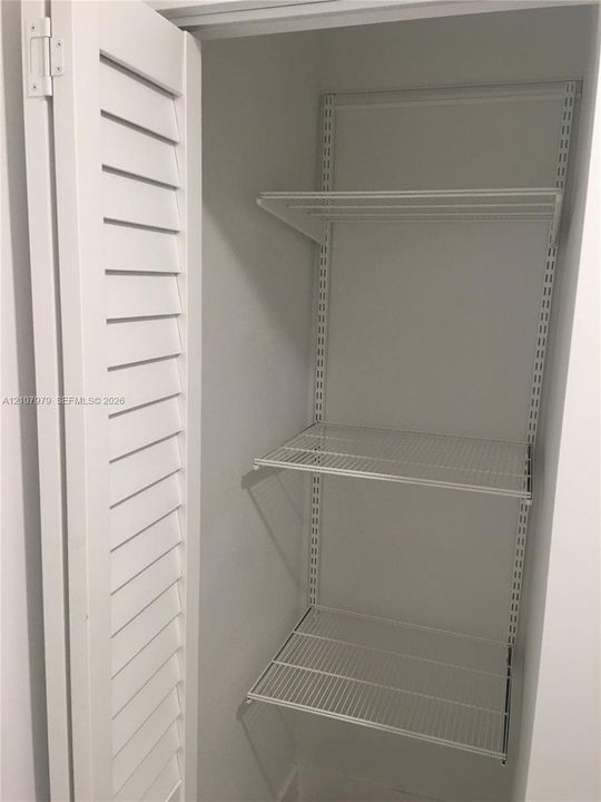 Storage closet featuring white louvered doors and adjustable wire shelving units