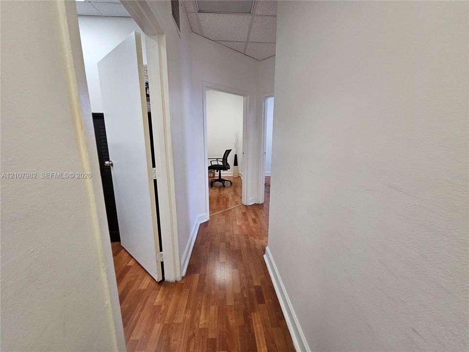 Hallway featuring wood-finish flooring, white doors, and a drop ceiling