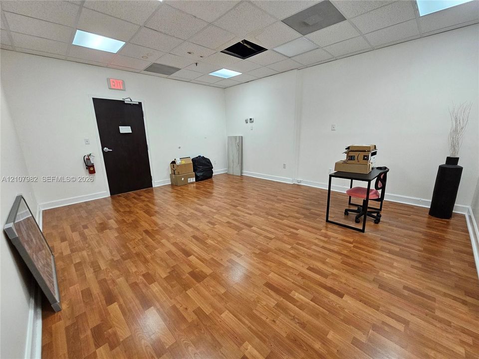 Open floor plan room featuring wood-finish flooring, a suspended acoustic tile ceiling, and inset panel lighting
