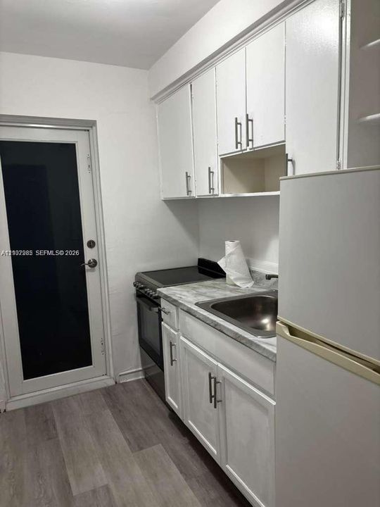 Kitchen featuring white cabinetry with brushed metal hardware, stone-finish countertops, stainless steel sink, and wood-finish flooring