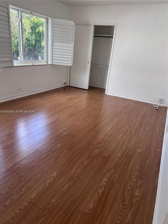 Room featuring wood-finish flooring, white walls, plantation shutters, and a closet with sliding doors