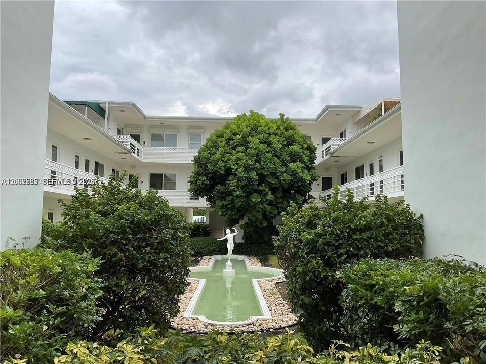 Courtyard featuring a decorative water fountain, central statue, surrounding mature shrubbery, and multi-level balconies
