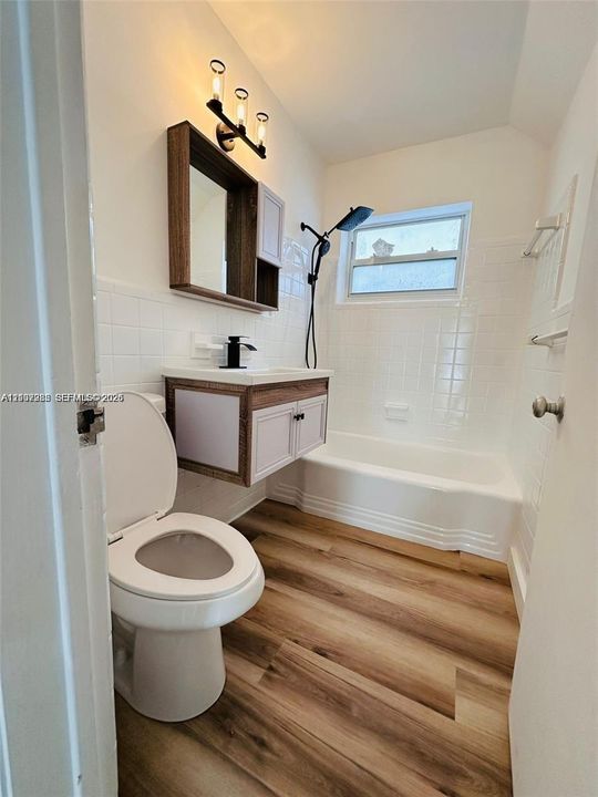 Bathroom featuring a floating vanity with a dark-finish frame, wood-finish flooring, a white tiled shower surround, and a wall-mounted light fixture with three glass shades