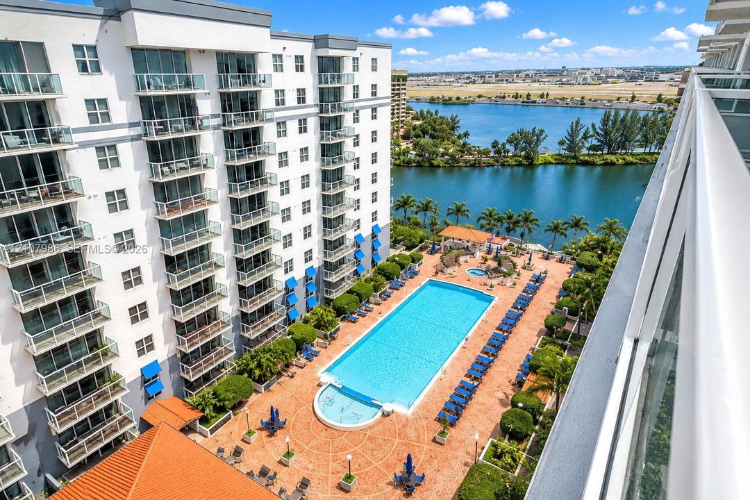 Multi-story building featuring private glass-railed balconies, expansive swimming pool, landscaped sun deck with paved hardscaping, and water frontage