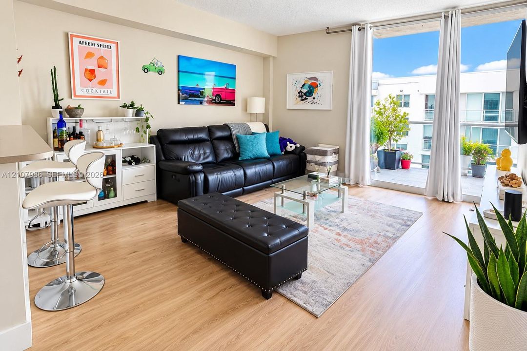 Living area featuring wood-finish flooring, floor-to-ceiling glass door, and a balcony with a glass railing