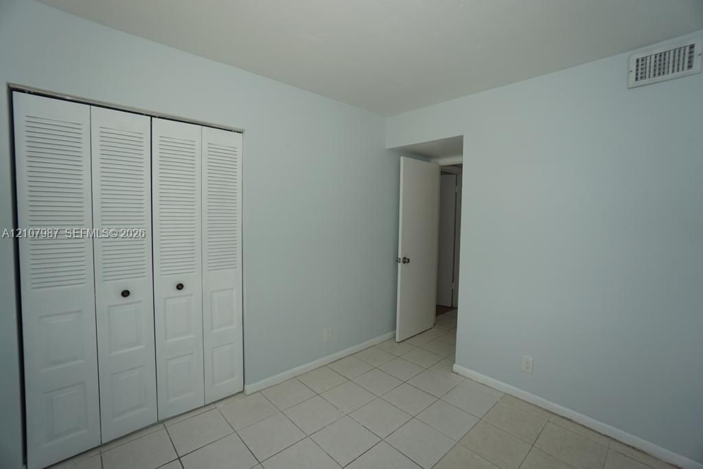 Neutral-toned room featuring light-colored tile flooring and a double-door closet with louvered panels