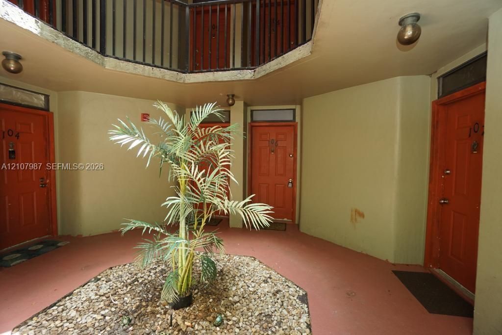 Enclosed courtyard featuring multi-level corridors with black metal railings, central rock-fill garden bed, and four solid-core entry doors with transom windows