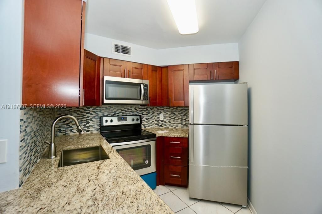 Kitchen featuring shaker-style wood cabinetry, stainless steel appliances, stone-finish countertops, tile backsplash, and a deep-basin sink with a gooseneck faucet