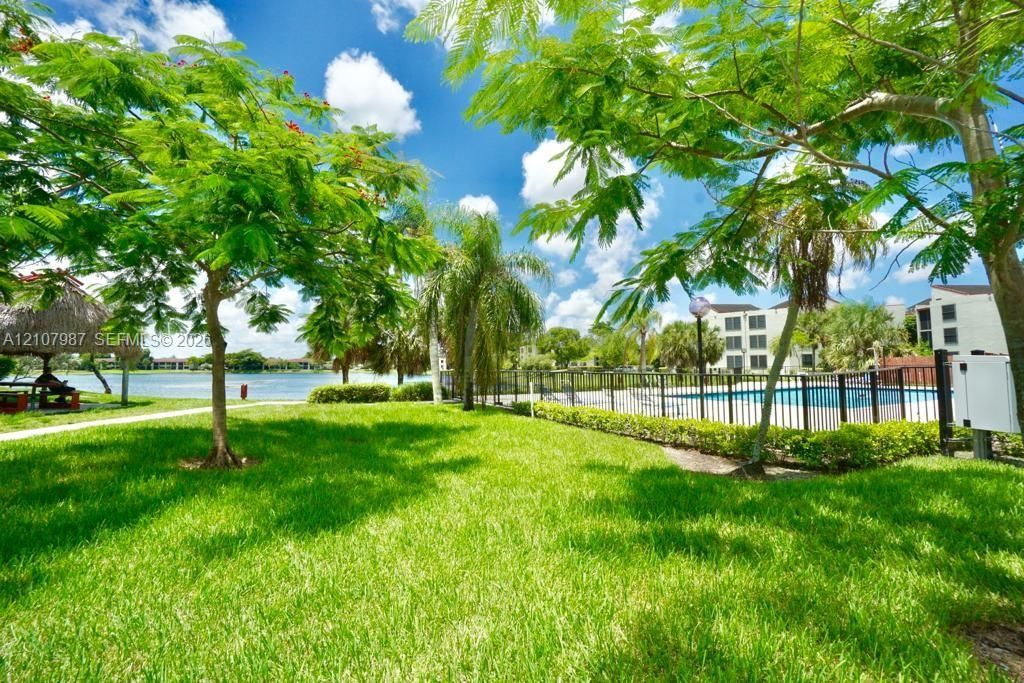 Expansive grounds featuring a manicured lawn, mature trees, a fenced swimming pool, and a thatch-roof structure situated on the water's edge