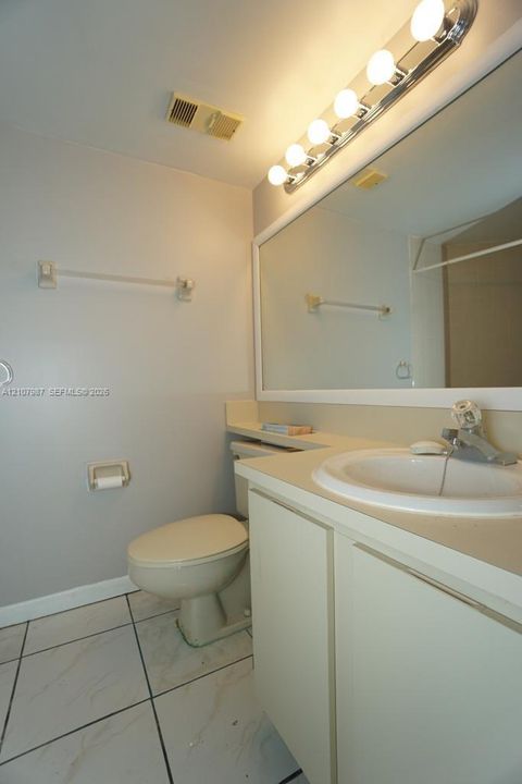 Bathroom featuring white tile flooring, vanity with integrated basin, large rectangular wall-mounted mirror, and multi-bulb vanity light fixture