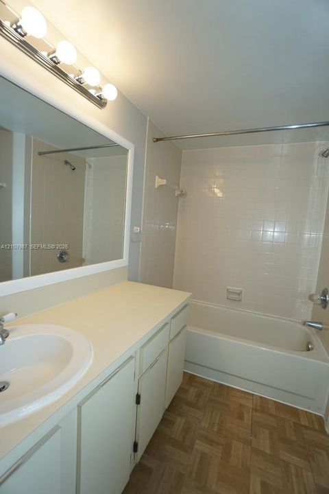 Bathroom featuring a vanity with a solid-surface countertop, an integrated sink, a full-width wall mirror, tile-surround bathtub, and wood-finish flooring