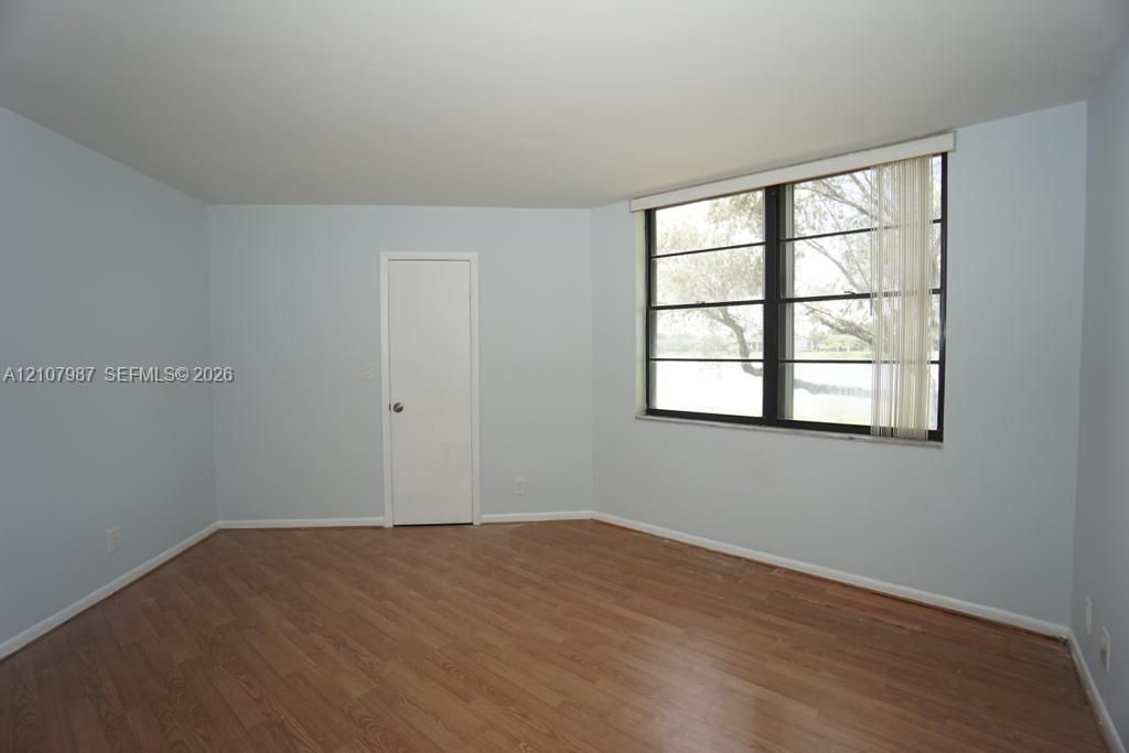 Room featuring wood-finish flooring, light blue walls, and a large multi-pane window with vertical blinds