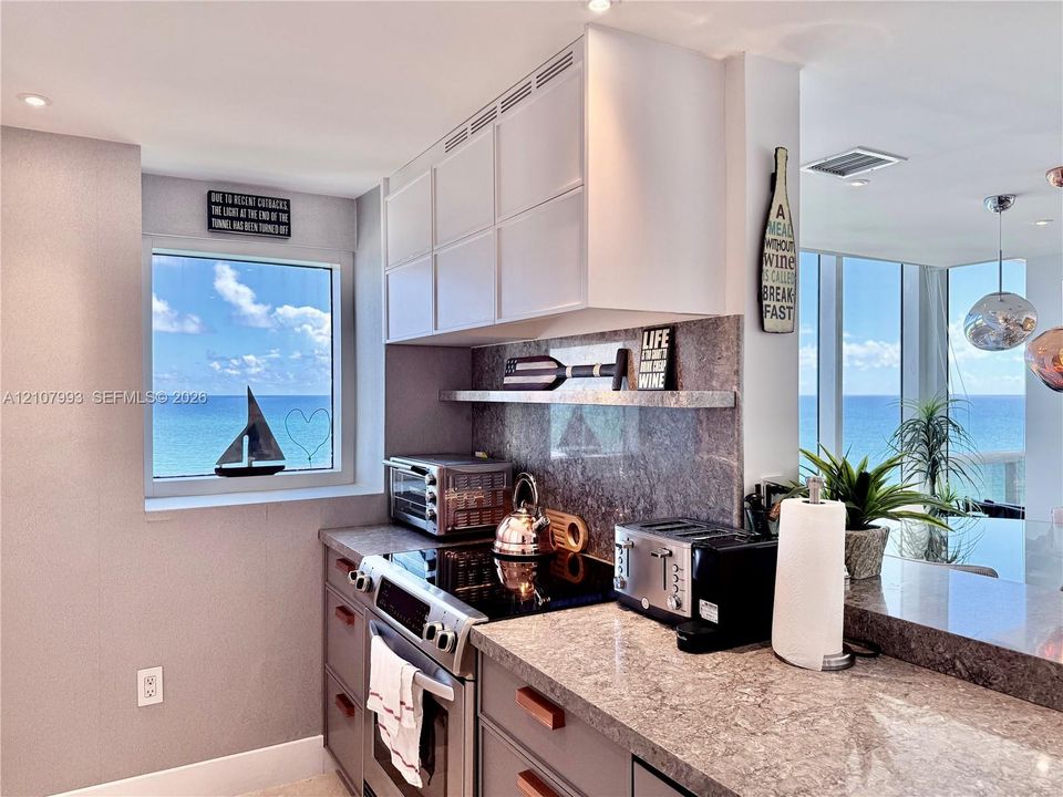 Kitchen featuring white upper cabinetry, grey lower cabinetry, stone-finish countertops, stone-finish backsplash, and built-in stainless steel range