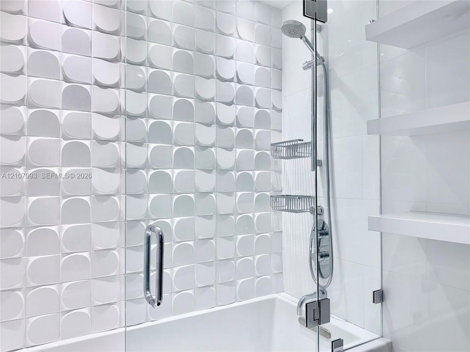 Textured three-dimensional wall tile, glass-enclosed shower, adjustable height handheld shower head, and built-in floating shelves