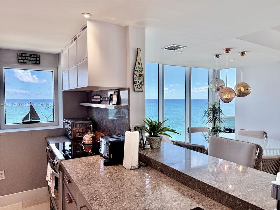 Kitchen featuring a stone-surface breakfast bar, slab backsplash, light-toned cabinetry, recessed lighting, and floor-to-ceiling windows with ocean scenery