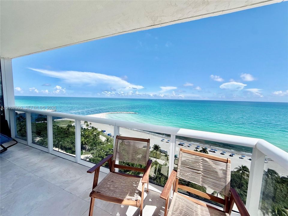 Covered balcony featuring oversized neutral floor tiling and white-framed glass panel railings with an open-air oceanfront exposure