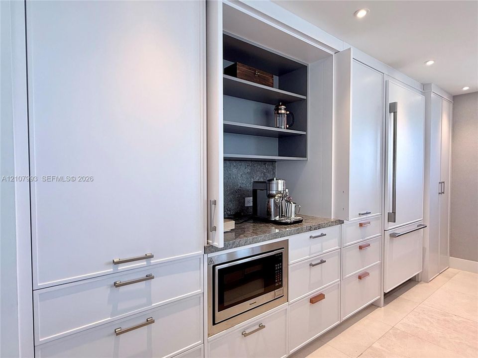 Floor-to-ceiling cabinetry with custom millwork, integrated refrigerator, stone countertop, built-in microwave, and recessed lighting