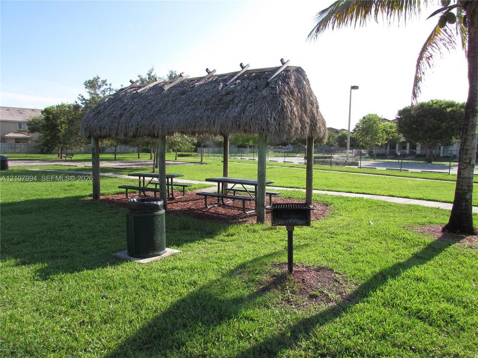 Open-air pavilion with a thatched roof, metal pedestal grill, and manicured lawn space