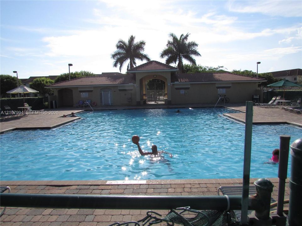 Community swimming pool featuring a brick paver deck, tiled roofing, and integrated palm tree landscaping