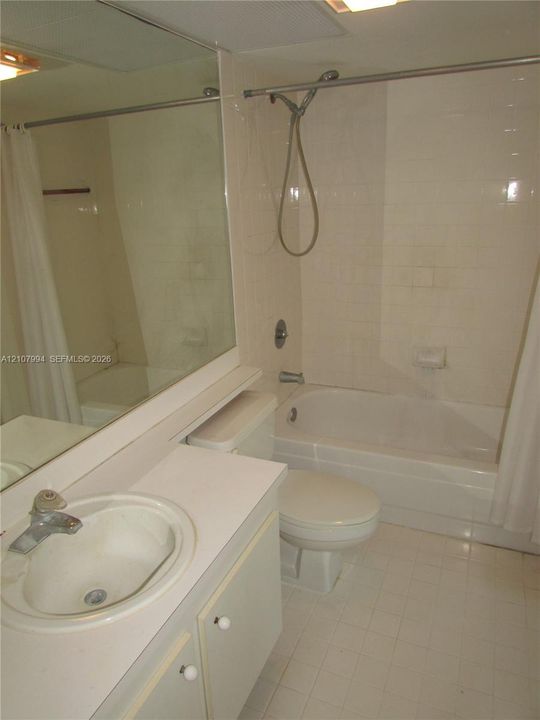 Full-width vanity with integrated sink, expansive wall-mounted mirror, white ceramic tile flooring, and a combined tub and shower enclosure with a handheld fixture