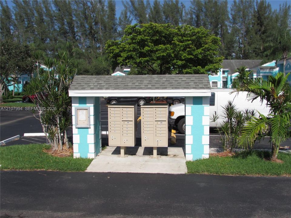 Covered mail station featuring twin metallic parcel units, concrete foundation, and decorative block pillars with shingled roofing