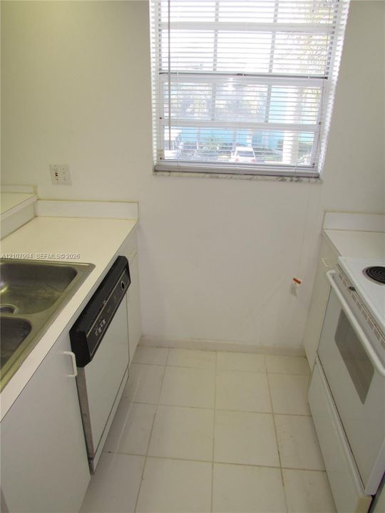 Kitchen featuring white cabinetry, solid-surface countertops, dual-basin stainless steel sink, integrated dishwasher, and tile flooring